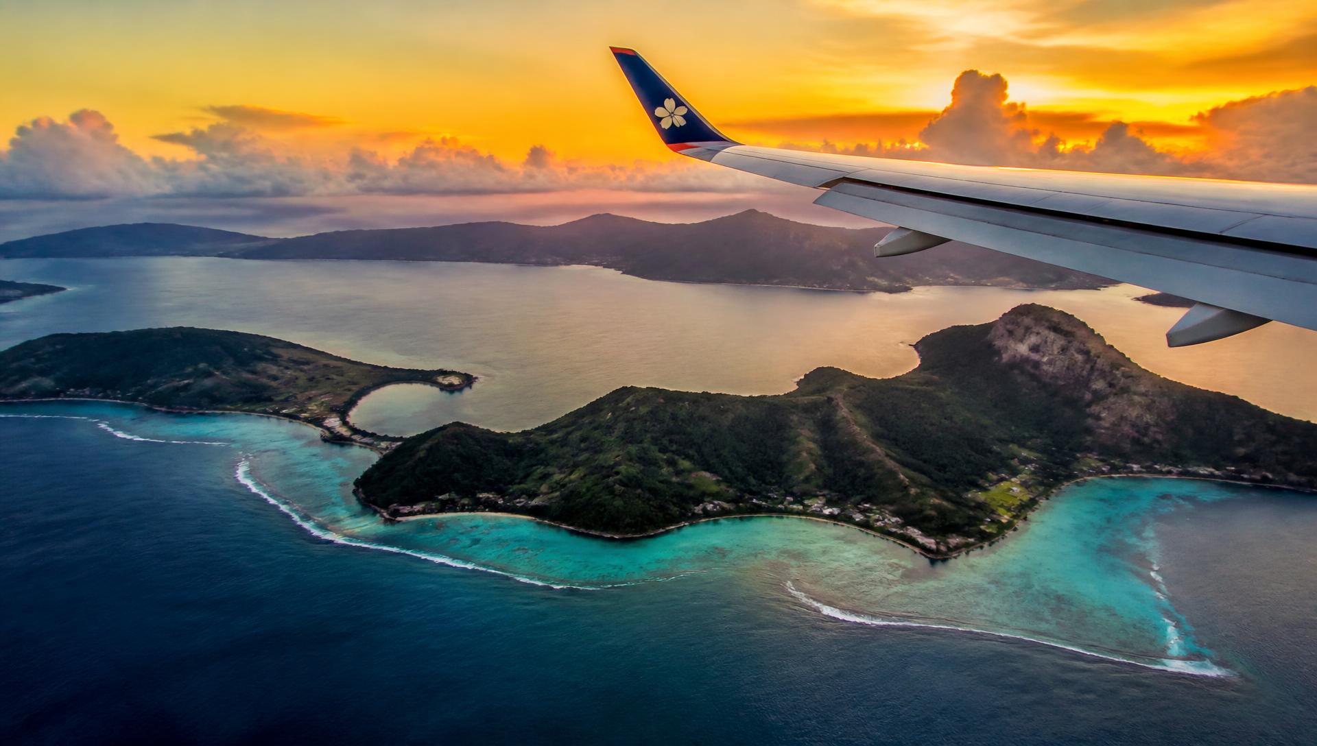 Airplane wing above tropical islands at sunset